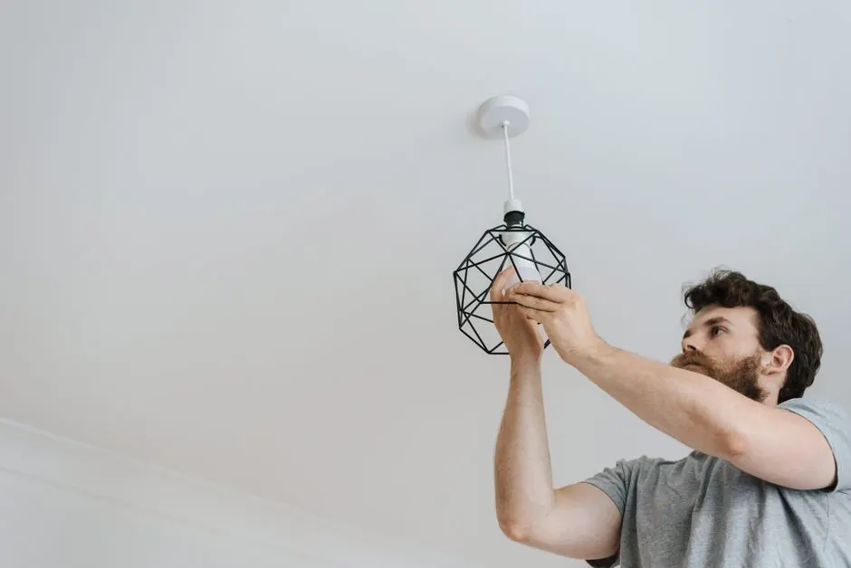 From below of male screwing light bulb into new fashionable lamp during renovation work in apartment