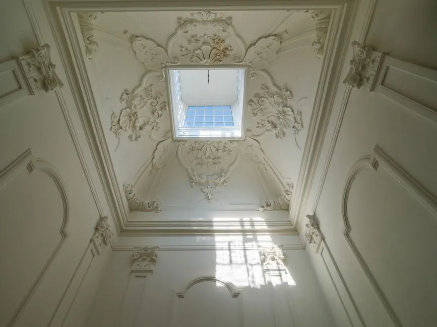 Luxurious ornate ceiling with an elegant skylight casting soft light indoors.